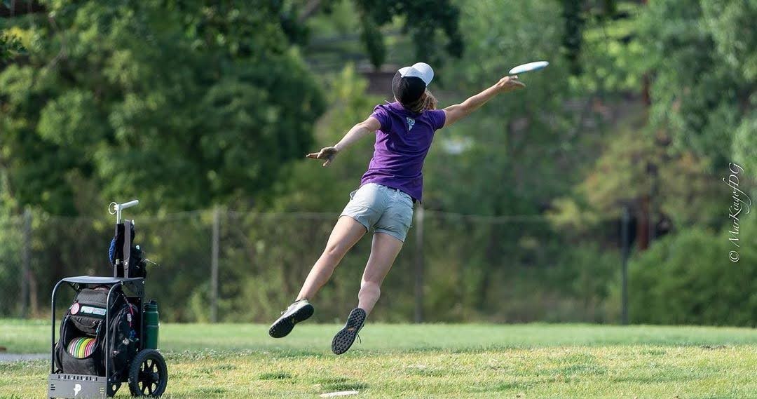 An action photo taking by Marking of DG of Disc golfer Paige Pierce jump putting at full extension while releasing her putter.