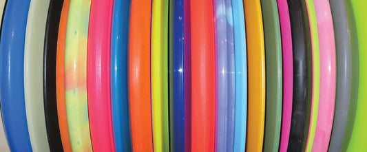 A side view of a stack of disc golf discs in a variety of plastics and colors.