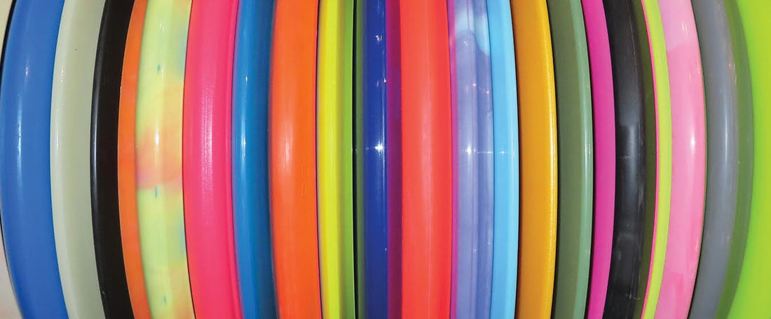 A side view of a stack of disc golf discs in a variety of plastics and colors.