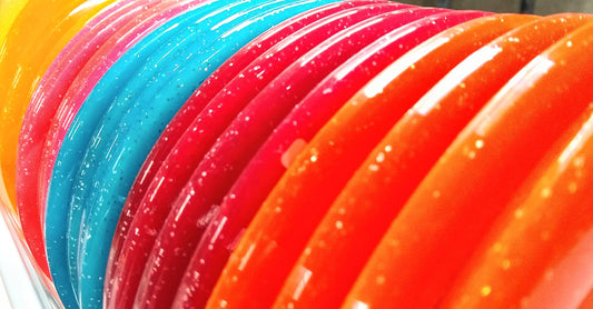 Closeup view of a row of orange, red, blue, and yellow sparkly disc golf discs edges.