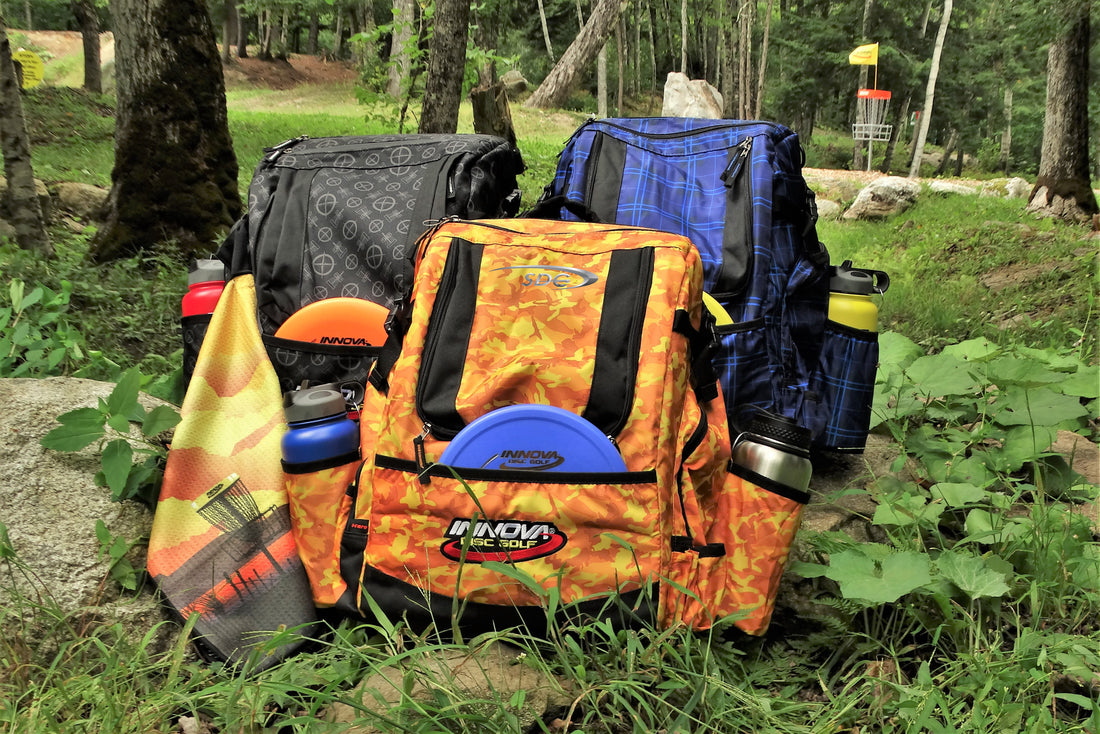 Three Innova Hero Pack Disc Golf Bags with accessories Sitting on the course at Sabattus Disc Golf 