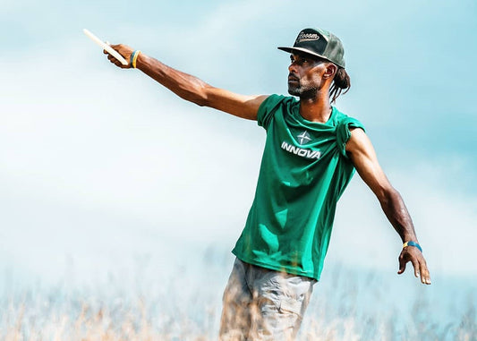 professional disc golfer philo brathwaite wearing a green shirt with the short sleeves bunched up aims his disc before a drive.