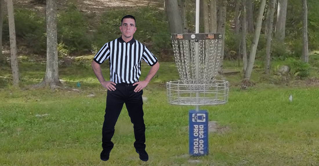 Black & white Striped Shirted Referee standing next to a disc golf basket
