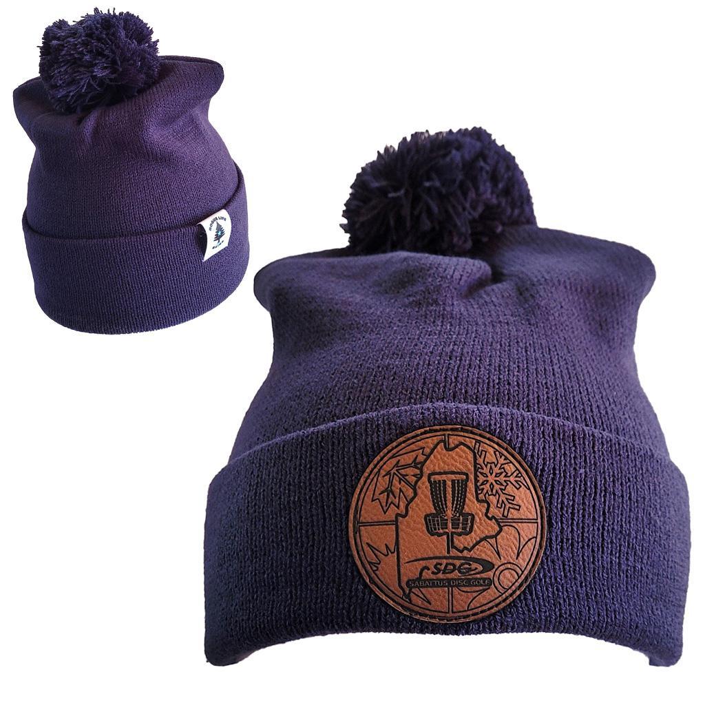 True Navy  Knit Pom Pom Beaning with SDG Sabattus Disc Golf Laser Engraved on leather patch that is sewn to the front of the hat, also a back view of the hat with the Rogue Life Maine logo on a small white tag sewn to the hat rim 